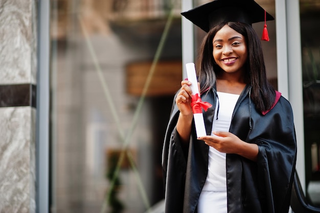 Jonge vrouwelijke Afro-Amerikaanse student met diploma poseert buitenshuisxA