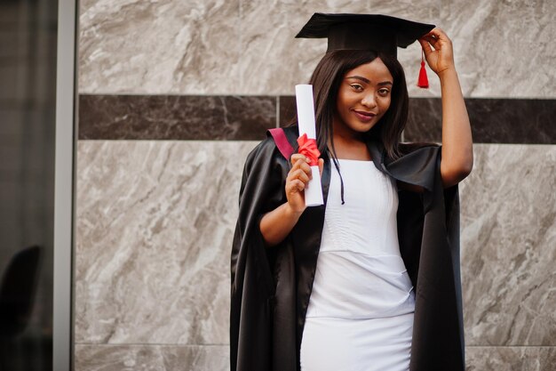 Jonge vrouwelijke Afro-Amerikaanse student met diploma poseert buitenshuisxA