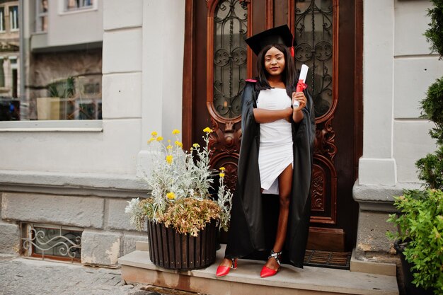 Jonge vrouwelijke Afro-Amerikaanse student met diploma poseert buitenshuisxA