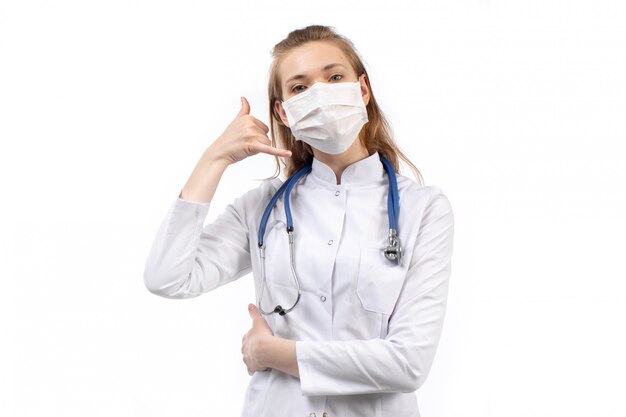 jonge vrouwelijke arts in witte medische pak in witte beschermend masker stethoscoop poseren op de witte