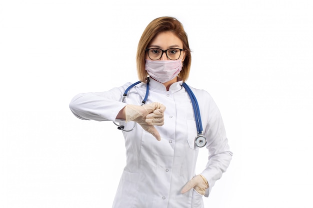 jonge vrouwelijke arts in witte medische pak met stethoscoop in wit beschermend masker in tegenstelling tot teken op de witte tonen