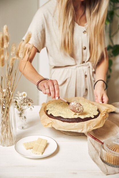 Jonge vrouwelijke bakker die een heerlijke chocoladetaart maakt met room op een witte tafel