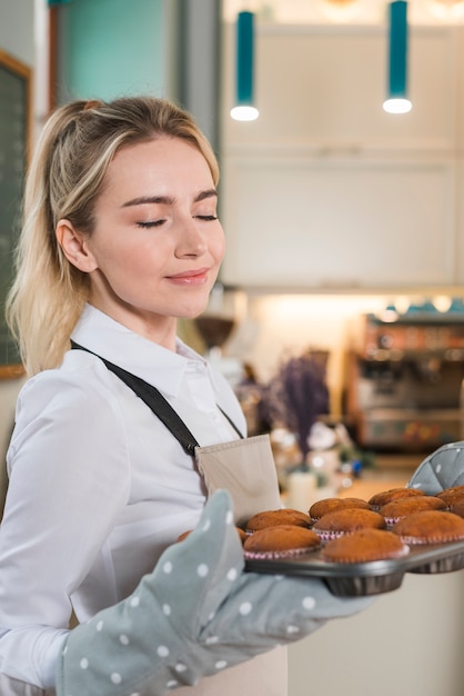 Jonge vrouwelijke bakker die van de prettige geur van gebakken muffins geniet