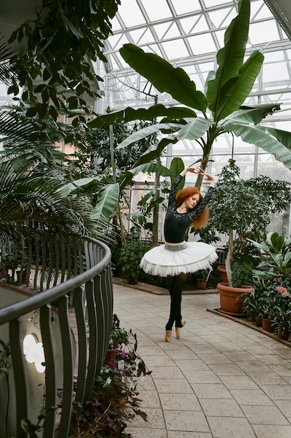 Jonge vrouwelijke ballerina die danst in een botanische tuin binnenshuis