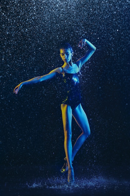 Jonge vrouwelijke balletdanser presteren onder waterdruppels en spray. Kaukasisch model dansen in neonlichten. Aantrekkelijke vrouw. Ballet en hedendaags choreografieconcept. Creatieve kunstfoto.