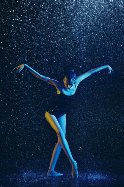 Jonge vrouwelijke balletdanser presteren onder waterdruppels en spray. Kaukasisch model dansen in neonlichten. Aantrekkelijke vrouw. Ballet en hedendaags choreografieconcept.