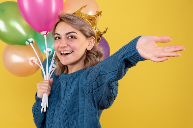 Gratis foto jonge vrouwelijke bedrijf ballonnen in kroon op geel