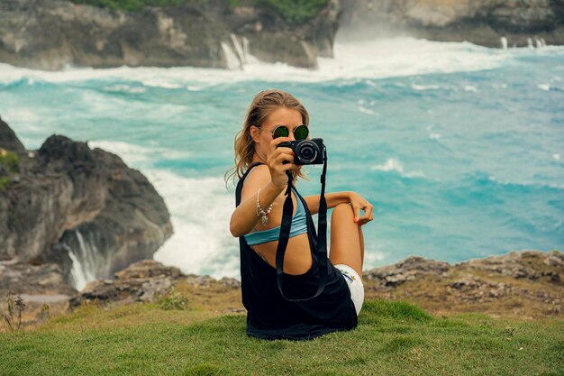 Jonge vrouwelijke fotograaf-reiziger met een camera aan de rand van een klif maakt foto's van de natuur