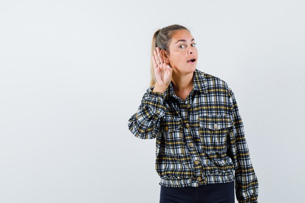 Jonge vrouwelijke hand achter het oor in shirt, korte broek en op zoek nieuwsgierig, vooraanzicht.