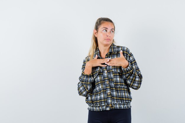 Jonge vrouwelijke hand in hand op de borst in shirt, korte broek en peinzend, vooraanzicht kijken.