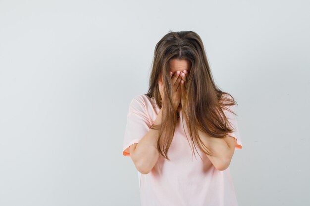 Jonge vrouwelijke hand in hand op gezicht in roze t-shirt en op zoek depressief, vooraanzicht.