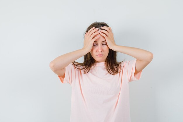 Jonge vrouwelijke hand in hand op het hoofd in roze t-shirt en op zoek vermoeid, vooraanzicht.