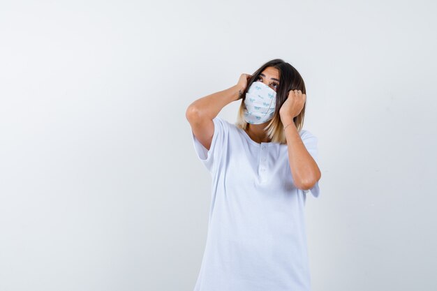 Jonge vrouwelijke hand in hand op het hoofd in t-shirt, masker en op zoek attent. vooraanzicht.