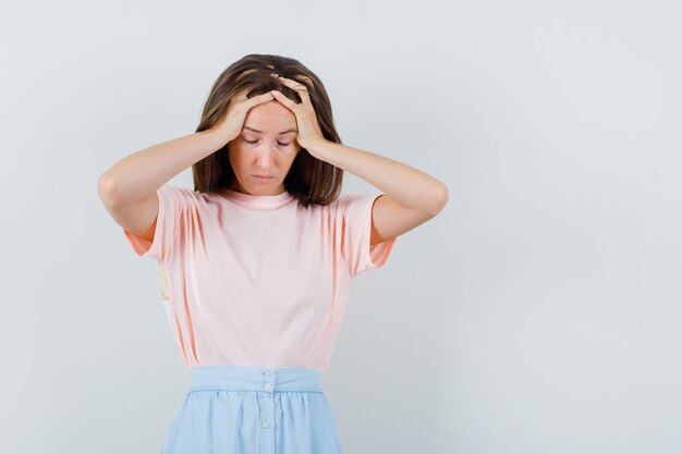 Jonge vrouwelijke hand in hand op het hoofd in t-shirt, rok en uitgeput op zoek. vooraanzicht.