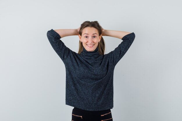 Jonge vrouwelijke hand in hand op het hoofd in zwarte blouse en op zoek vrolijk. vooraanzicht.