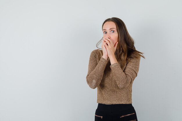 Jonge vrouwelijke hand in hand op mond in gouden blouse en op zoek opgewonden, vooraanzicht. ruimte voor tekst