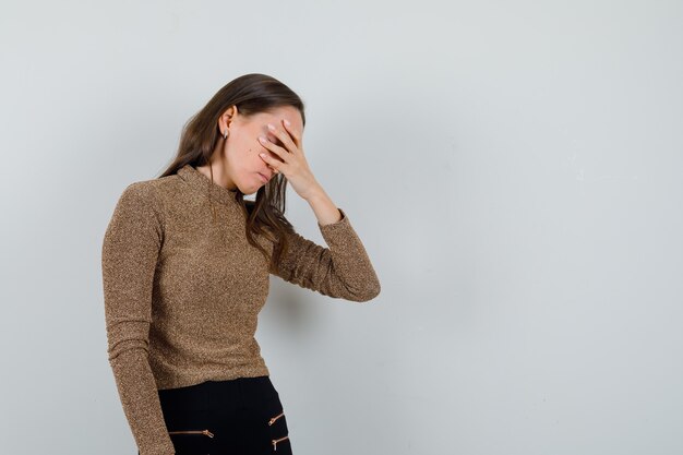 Jonge vrouwelijke hand in hand op ogen in gouden blouse en op zoek verveeld, vooraanzicht. ruimte voor tekst