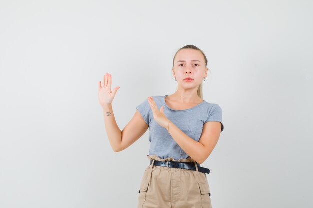 Jonge vrouwelijke handen op preventieve wijze in t-shirt, broek houden en angstig kijken. vooraanzicht.