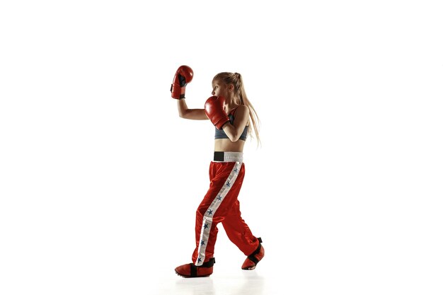 Jonge vrouwelijke kickboks vechter opleiding geïsoleerd op een witte muur. Kaukasisch blond meisje in rode sportkleding beoefenen in vechtsporten. Concept van sport, gezonde levensstijl, beweging, actie, jeugd.