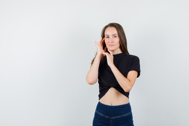 Jonge vrouwelijke kin en wang in zwarte blouse, broek aan te raken en op zoek verleidelijk