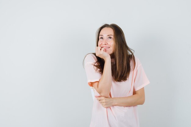 Jonge vrouwelijke kin op palm in roze t-shirt steunen en dromerig kijken. vooraanzicht.