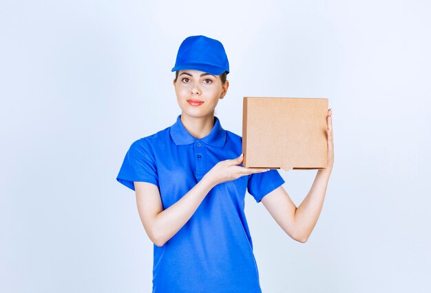 Jonge vrouwelijke koerier in blauw uniform met kartonnen doos op witte achtergrond.