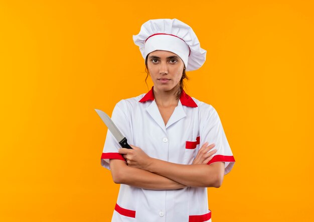 jonge vrouwelijke kok die chef-kok eenvormig bedrijfsmes draagt en handen op geïsoleerde gele muur met exemplaarruimte kruist