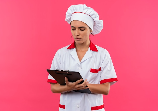 Jonge vrouwelijke kok die chef-kok eenvormige holding draagt en klembord met exemplaarruimte bekijkt