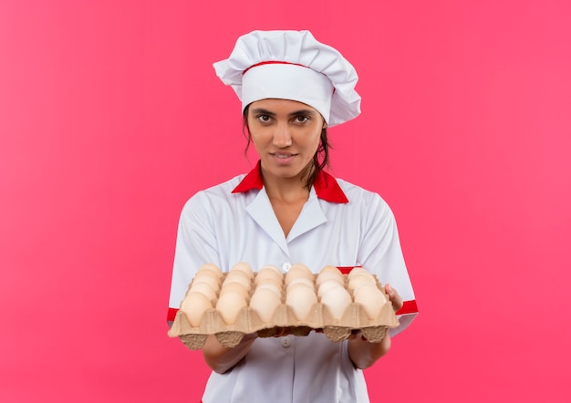 Gratis foto jonge vrouwelijke kok die chef-kok uniforme partij eieren op geïsoleerde roze muur met exemplaarruimte houdt