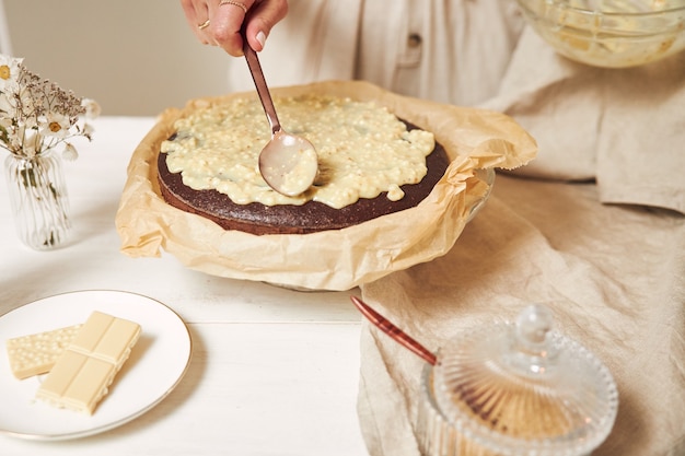 Jonge vrouwelijke kok die een heerlijke chocoladetaart maakt met room op een witte tafel