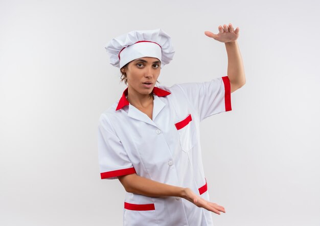 jonge vrouwelijke kok die eenvormige chef-kok draagt die grootte op geïsoleerde witte muur met exemplaarruimte toont
