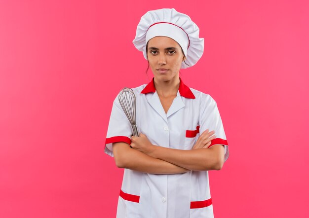jonge vrouwelijke kok die uniforme chef-kok draagt ?? die zwaait en de handen kruist op geïsoleerde roze muur met exemplaarruimte