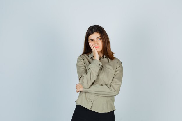 Jonge vrouwelijke leunende wang bij de hand in shirt, rok en boos kijken. vooraanzicht.