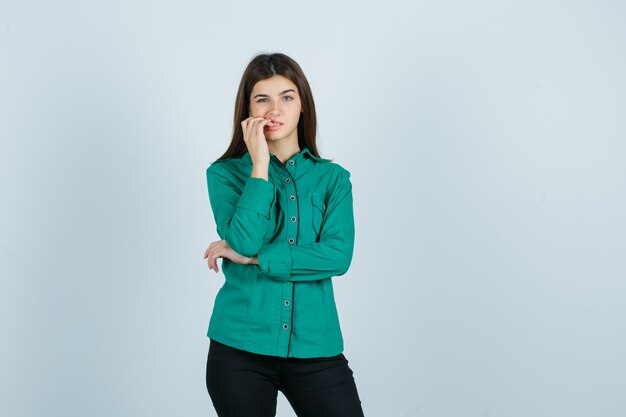 Jonge vrouwelijke nagels bijten in groen shirt, broek en op zoek verontrust. vooraanzicht.