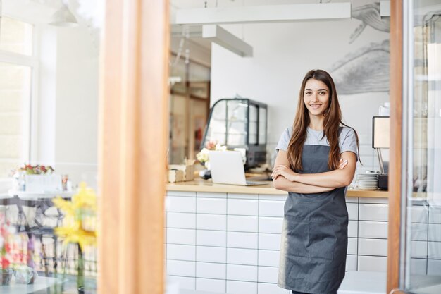 Jonge vrouwelijke ondernemer die een succesvol klein café runt Staande voor de koffiemachine met gekruiste armen