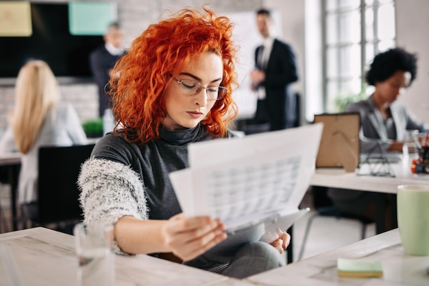 Jonge vrouwelijke ondernemer zit aan een bureau en analyseert bedrijfsrapporten op kantoor Er zijn mensen op de achtergrond