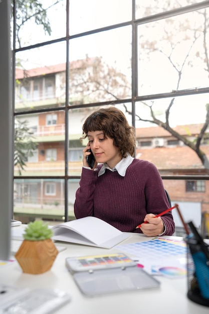 Jonge vrouwelijke ontwerper die aan de telefoon praat