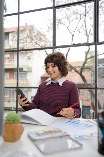 Gratis foto jonge vrouwelijke ontwerper die haar smartphone controleert