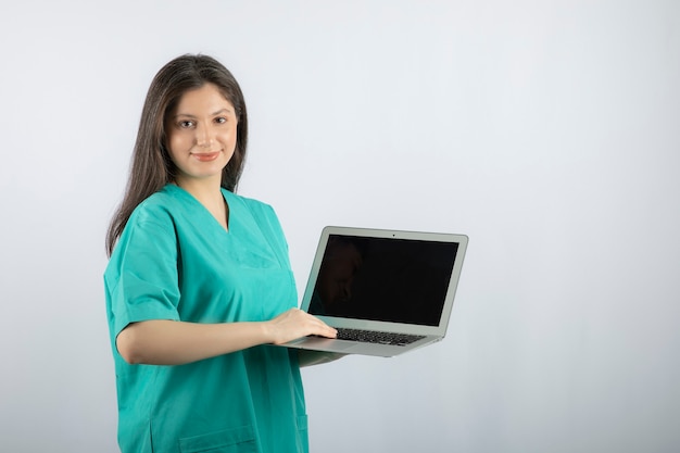 Jonge vrouwelijke verpleegster met laptop die zich op wit bevindt.