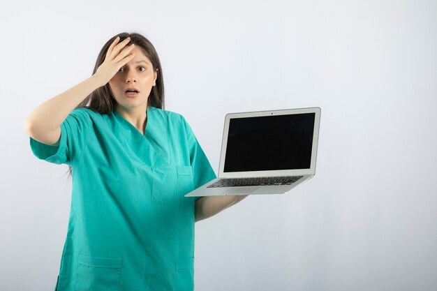 Jonge vrouwelijke verpleegster poseren met laptop en bang worden.