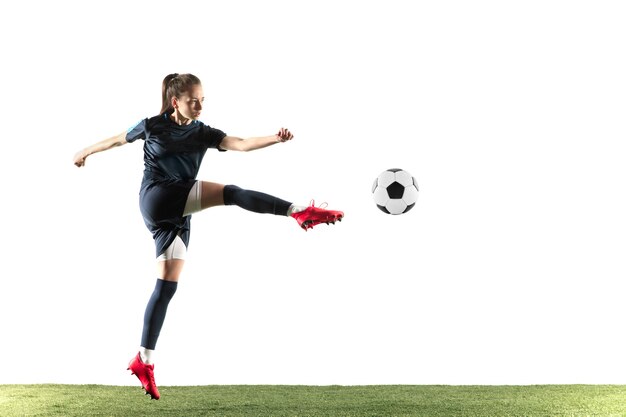 Jonge vrouwelijke voetbal of voetballer met lang haar in sportkleding en laarzen die bal voor het doel in sprong schoppen die op witte achtergrond wordt geïsoleerd. Concept van een gezonde levensstijl, professionele sport, hobby.