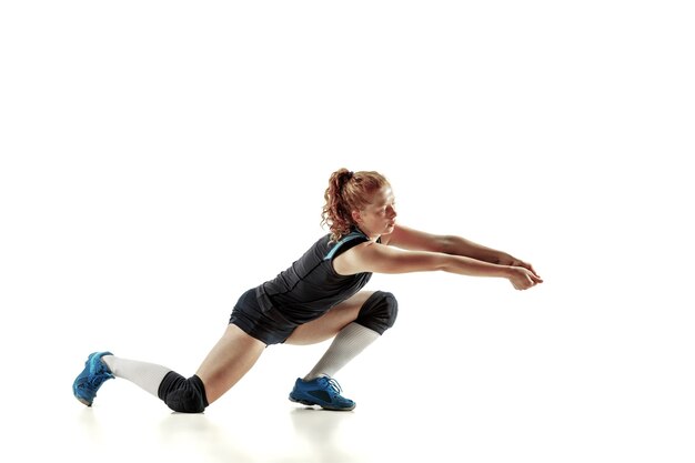 Jonge vrouwelijke volleyballspeler die op witte muur wordt geïsoleerd. Vrouw in sportuitrusting en schoenen of sneakers trainen en oefenen. Concept van sport, gezonde levensstijl, beweging en beweging.