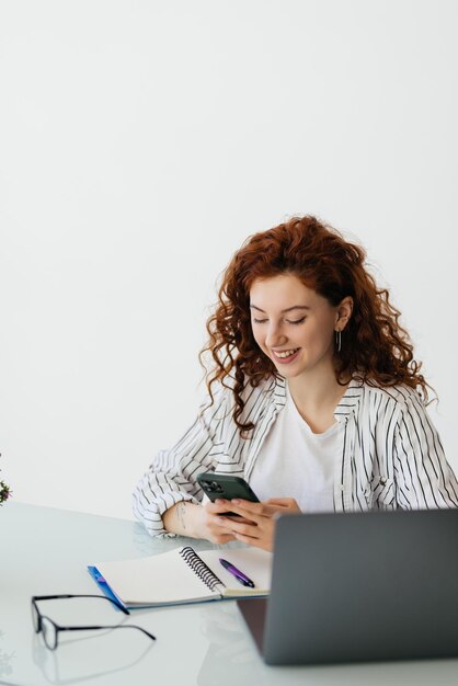 Jonge vrouwelijke werknemer zittend op het bureau en het gebruik van mobiele telefoon