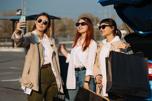 Jonge vrouwen bij de auto met boodschappentassen. Meisjes nemen selfie