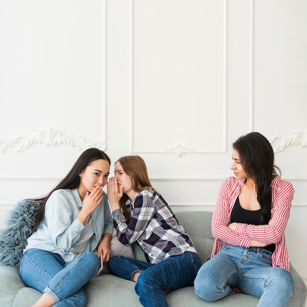 Jonge vrouwen die achter vriend fluisteren