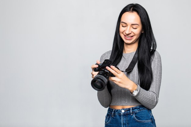 Jonge vrouwenfotograaf met camera die op grijze muur wordt geïsoleerd