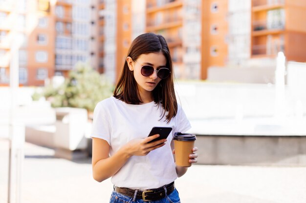 Jonge vrouwenlezing die telefoon met behulp van. Het vrouwelijke nieuws van de vrouwenlezing of het sms'en van sms op smartphone terwijl het drinken van koffie op onderbreking van het werk.