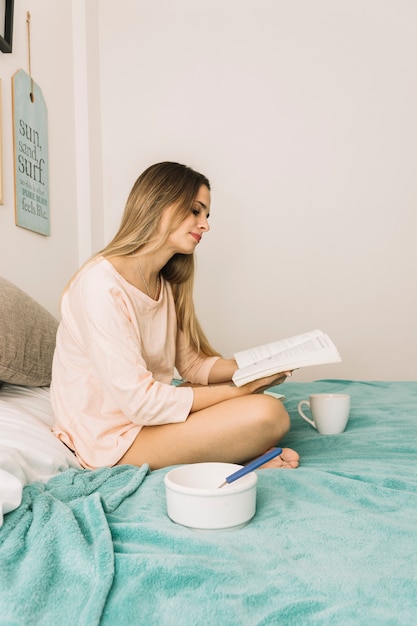 Gratis foto jonge vrouwenlezing tijdens ontbijt op bed