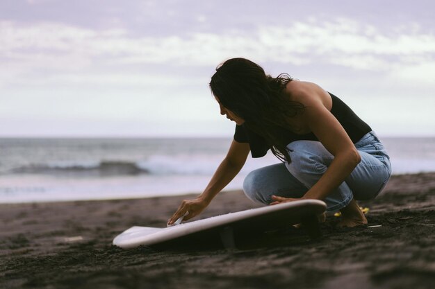 Jonge vrouwensurfer die een surfplank op het in de was zetten van de oceaan voorbereiden Vrouw met surfplank op de oceaan actieve levensstijl watersporten