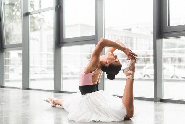 Jonge vrouwenzitting op vloer het praktizeren balletdans in dansstudio